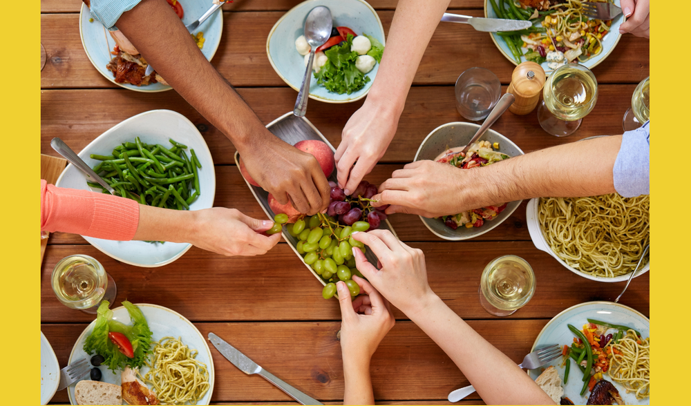 Arms of people reaching for fruit at the dining table.