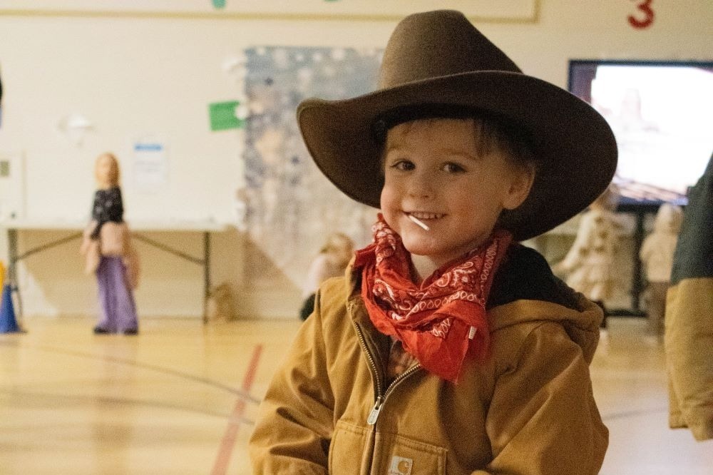 Student smiles with cowboy hat on and lollipop in his mouth