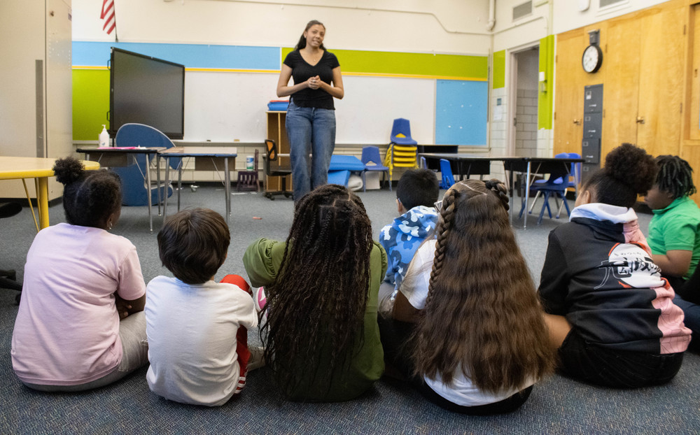 Group of students sits and listens to an older student speaking at the front of the room