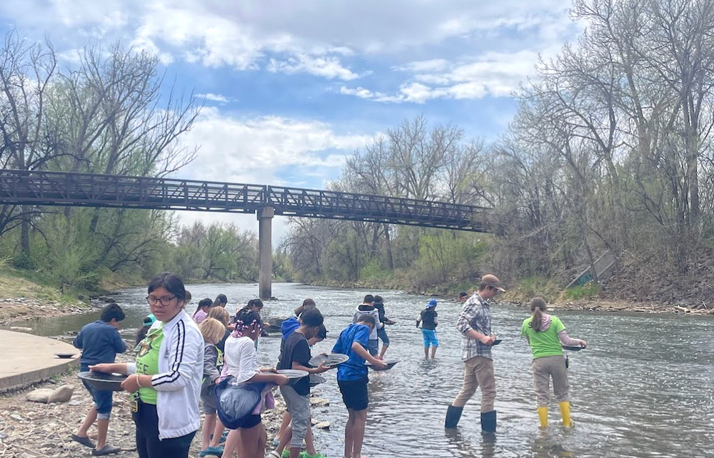 Students exploring a river with a bridge in the background