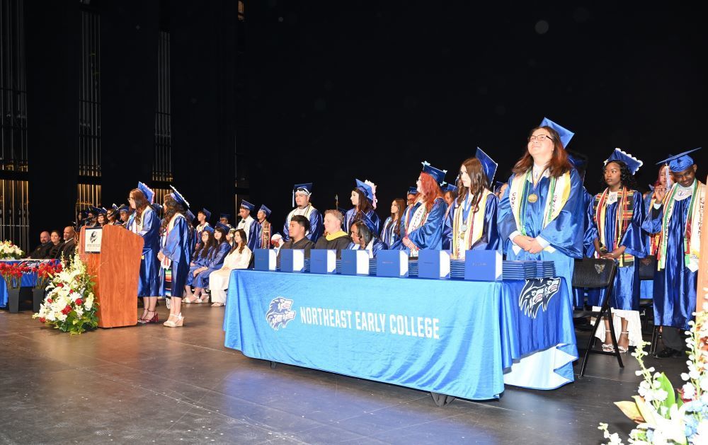 Stage full of NEC graduates in their caps and gowns.