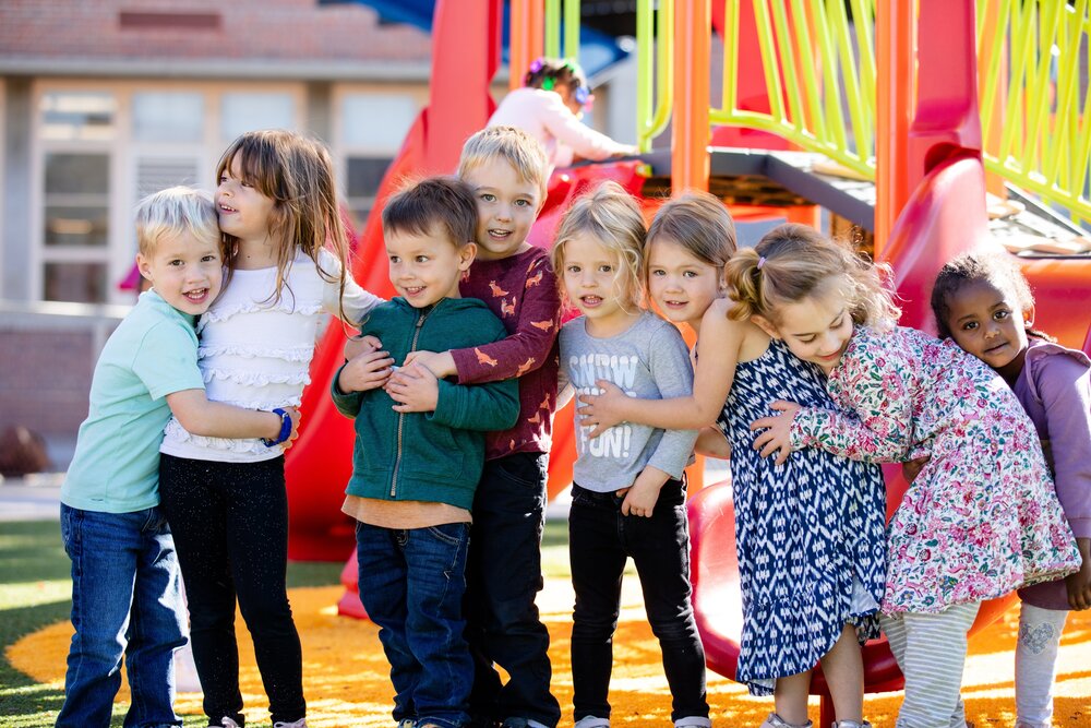 Kids join in a group hug in front of a playground