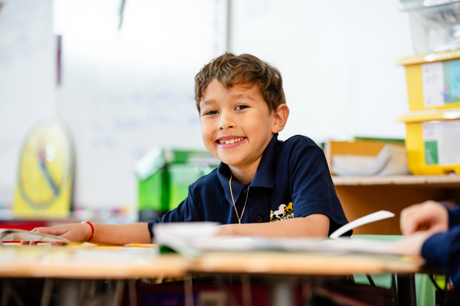 A student smiles at his desk during class.