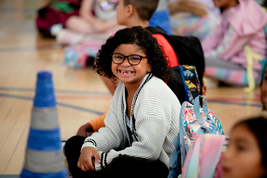 McMeen student smiles at the camera sitting on the floor in the gym