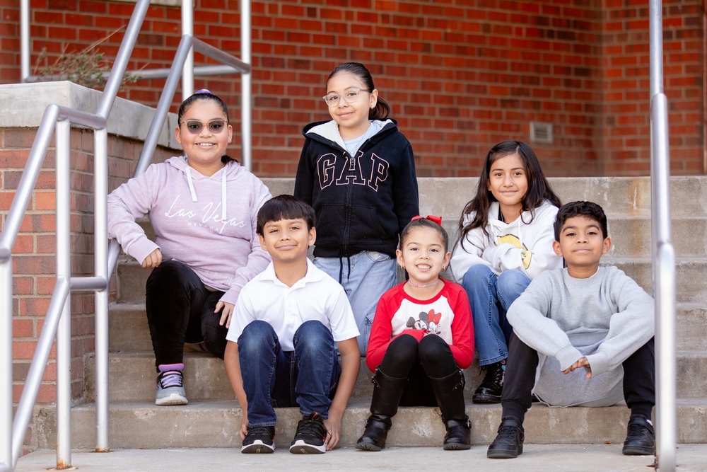 group of six students sitting on stairwell outside school building smiling