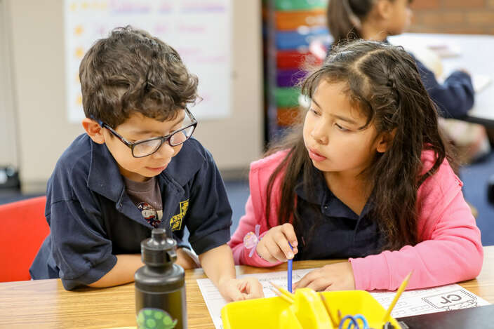 Two elementary students working together on a worksheet at a desk