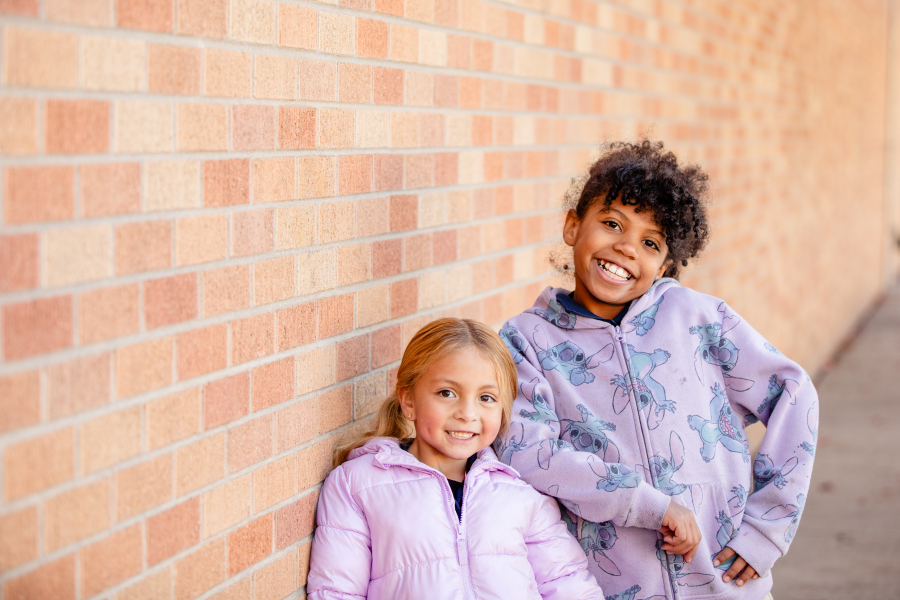 two students in front of a brick wall smiling 