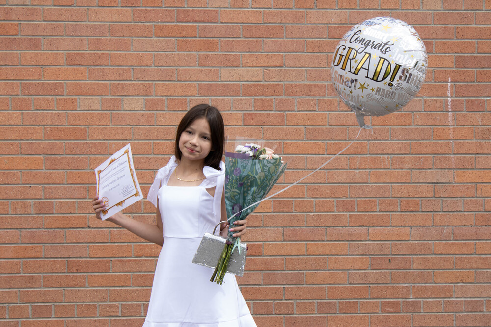 McMeen student smiles with a "congrats grad" balloon as she holds flowers and a certificate