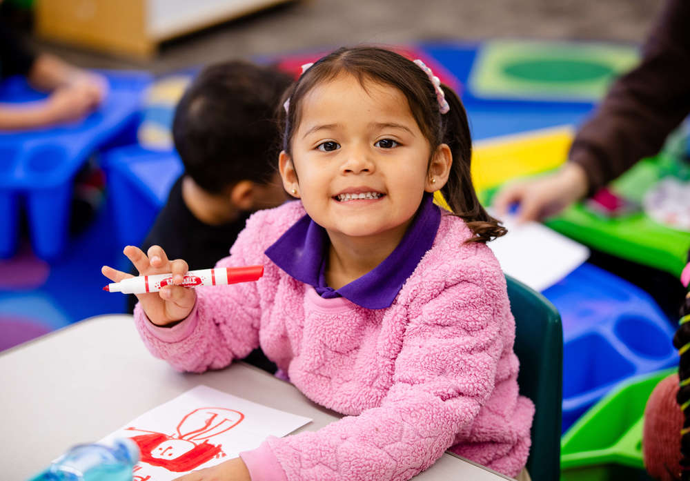 student smiling with a marker in hand at desk with art