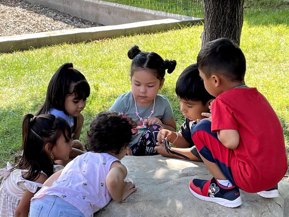 6 children sitting around a large rock