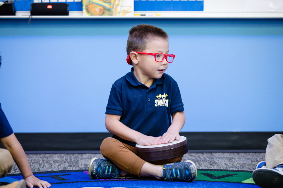 Student in red glasses playing a drum on his lap 