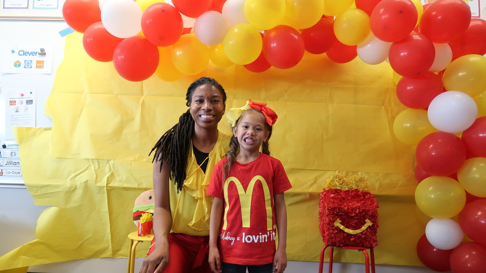 Student and adult standing in front of red, yellow, and white balloons