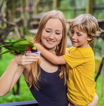 Woman with blond hair holds a colorful bird, child with short blond hair smiles at camera.