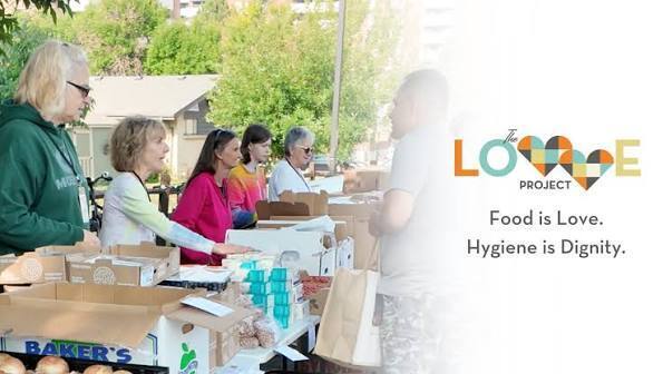 People gather around tables outdoors. Some individuals are helping others with food distribution.