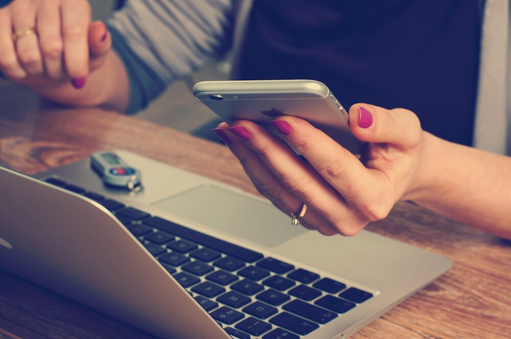 laptop in ffront of woman as she holds phone