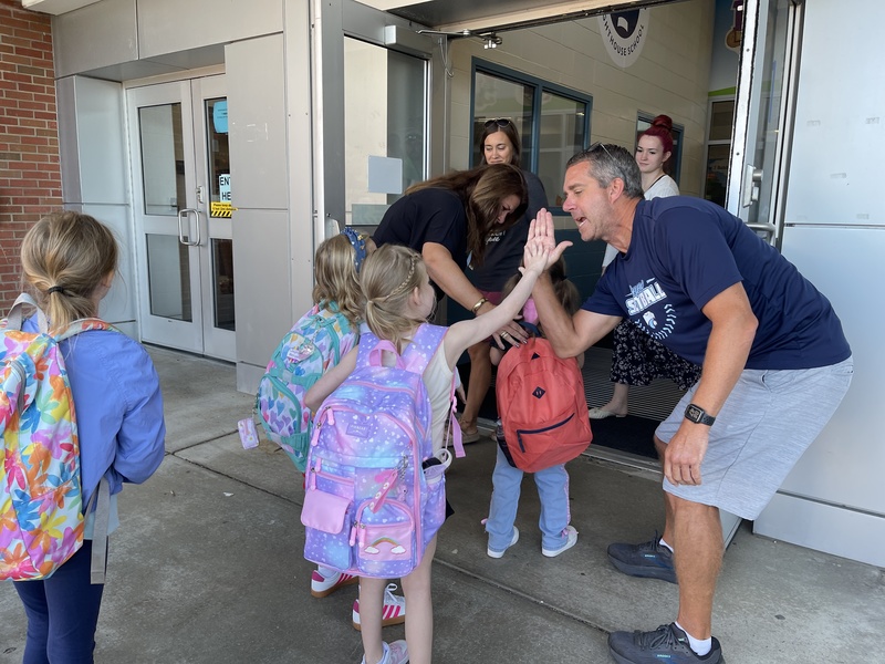 students high five staff member on their way into school