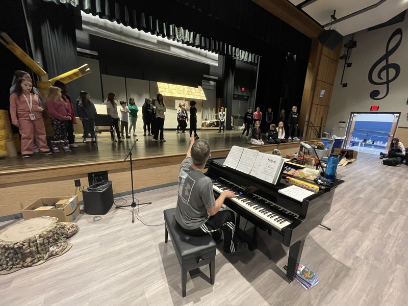 teacher on piano directing students on stage
