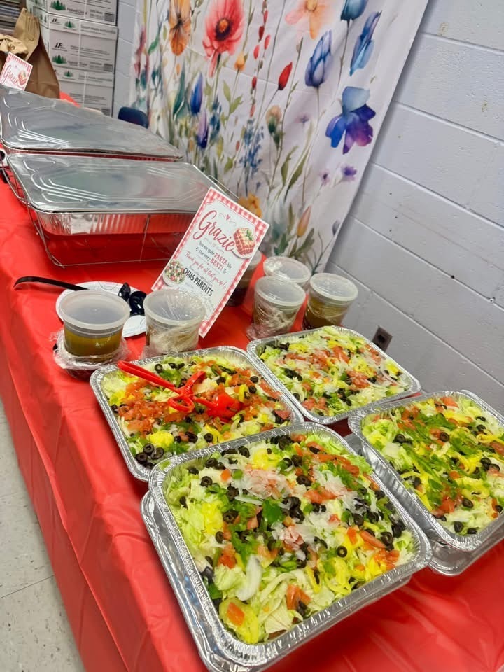 Table with trays of salad, trays of lasagna, and cups of sauce