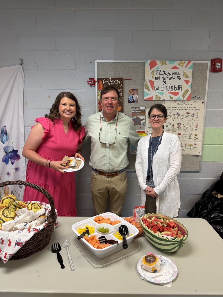 Two teachers standing with Josh McIntyre of Farm Bureau behind a table with McDonalds breakfast and a variety of fruit