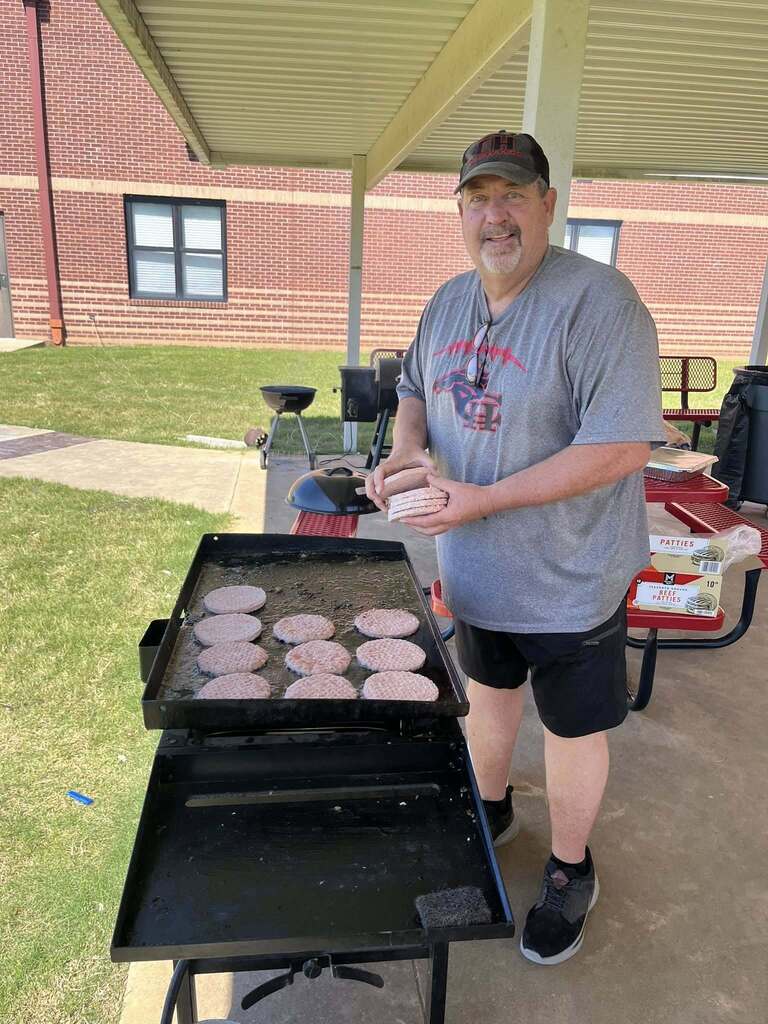 Coach Boren standing at a grill covered in cooking hamburgers