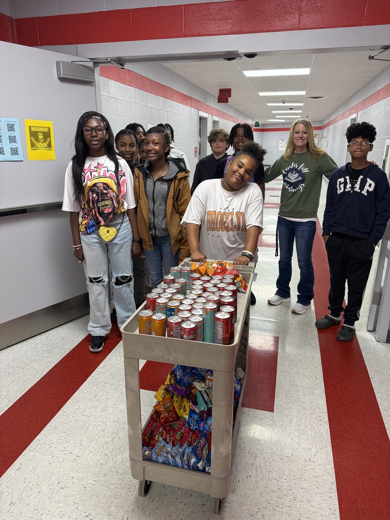 Several students and a teacher standing behind a two tiered cart with drinks on the top shelf and bags of chips on the bottom