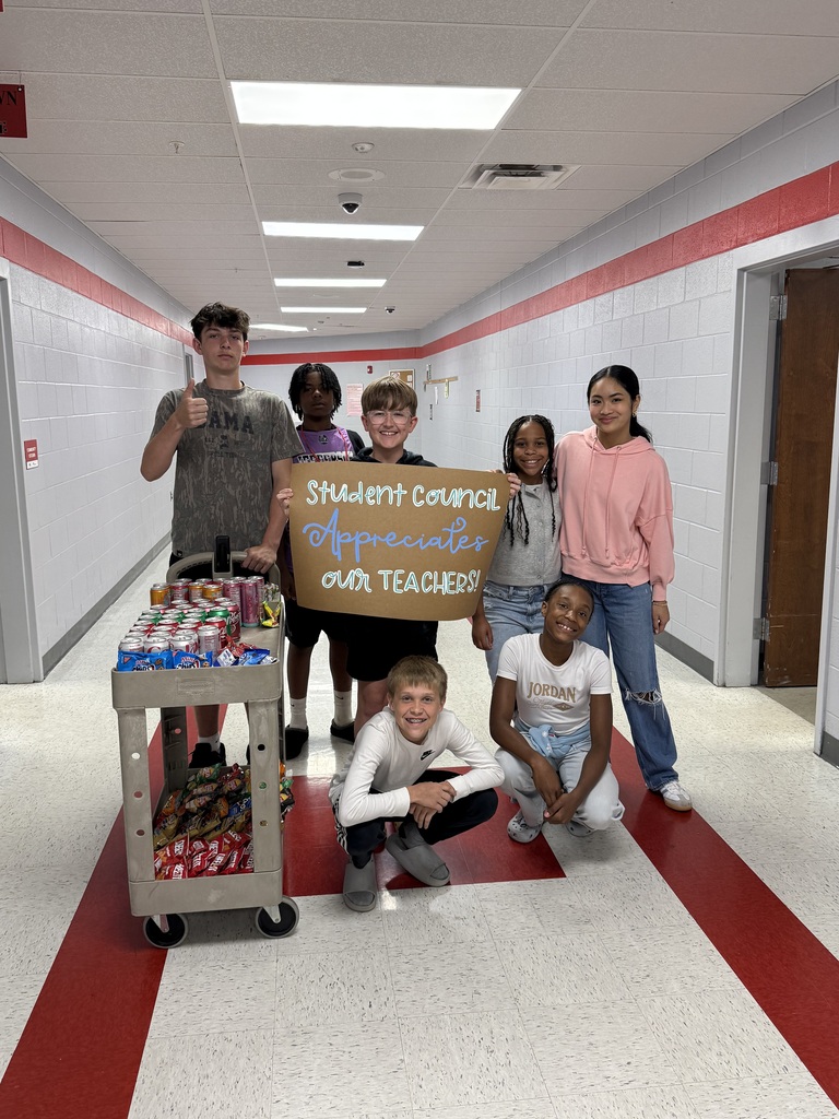 Students standing around a two tiered  snack cart with drinks on top and chips on the bottom holding a sign that says Student Council appreciates our teachers