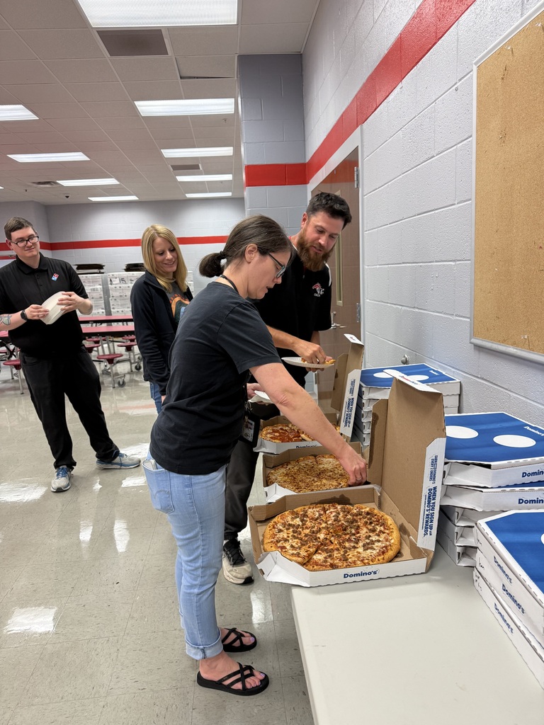 Two teachers getting Domino's Pizza from a table in a cafeteria while two others watch.