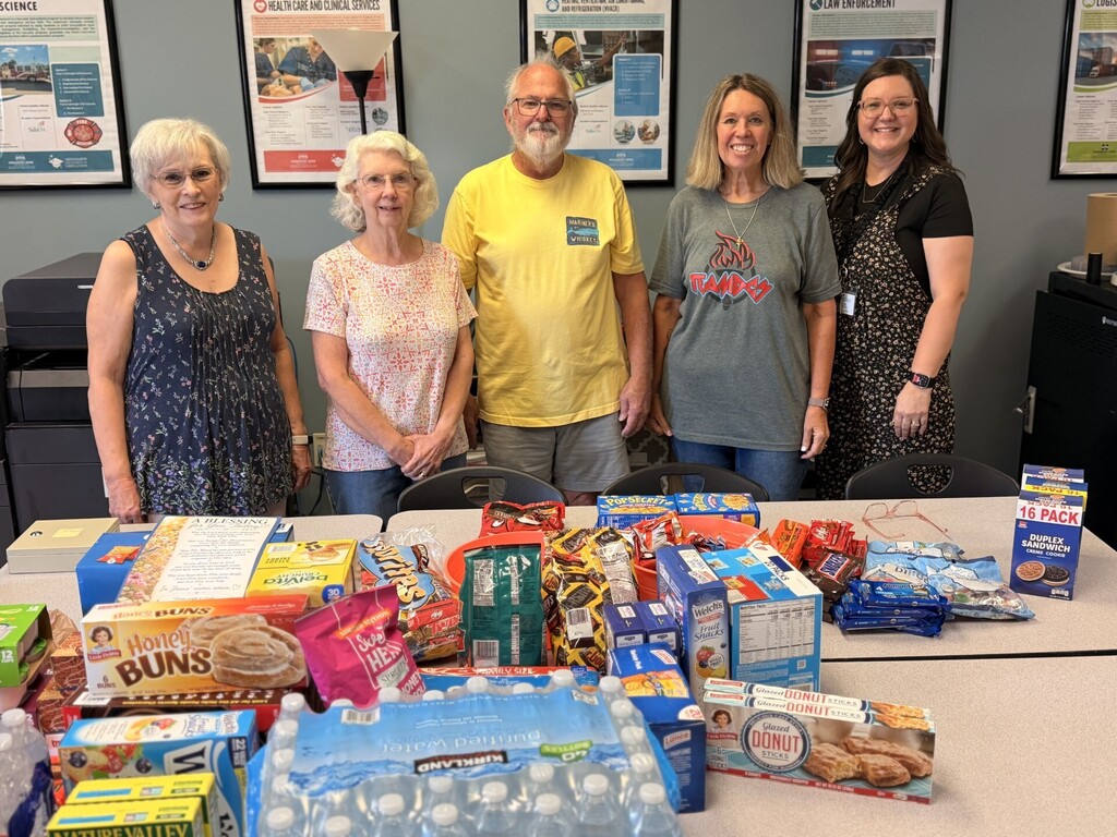 5 people standing behind table full of donated snacks