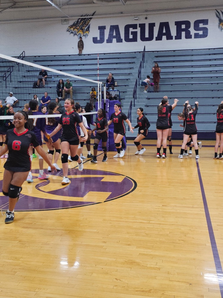 middle schools girls wearing black and red volleyball uniforms running out onto the court to start a game.
