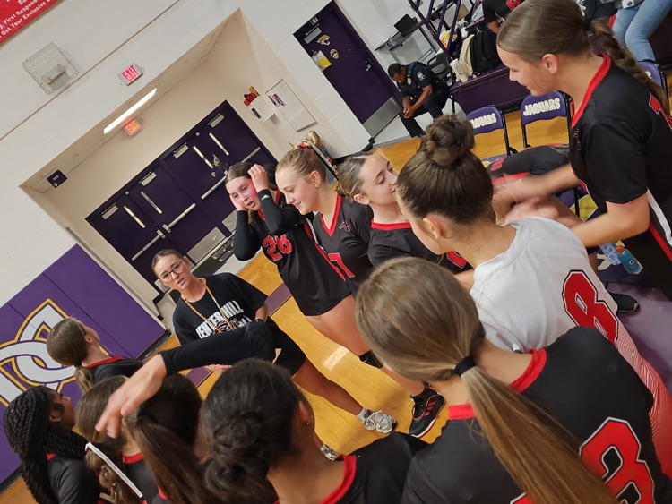 volley ball players wearing red and black uniforms in a huddle.