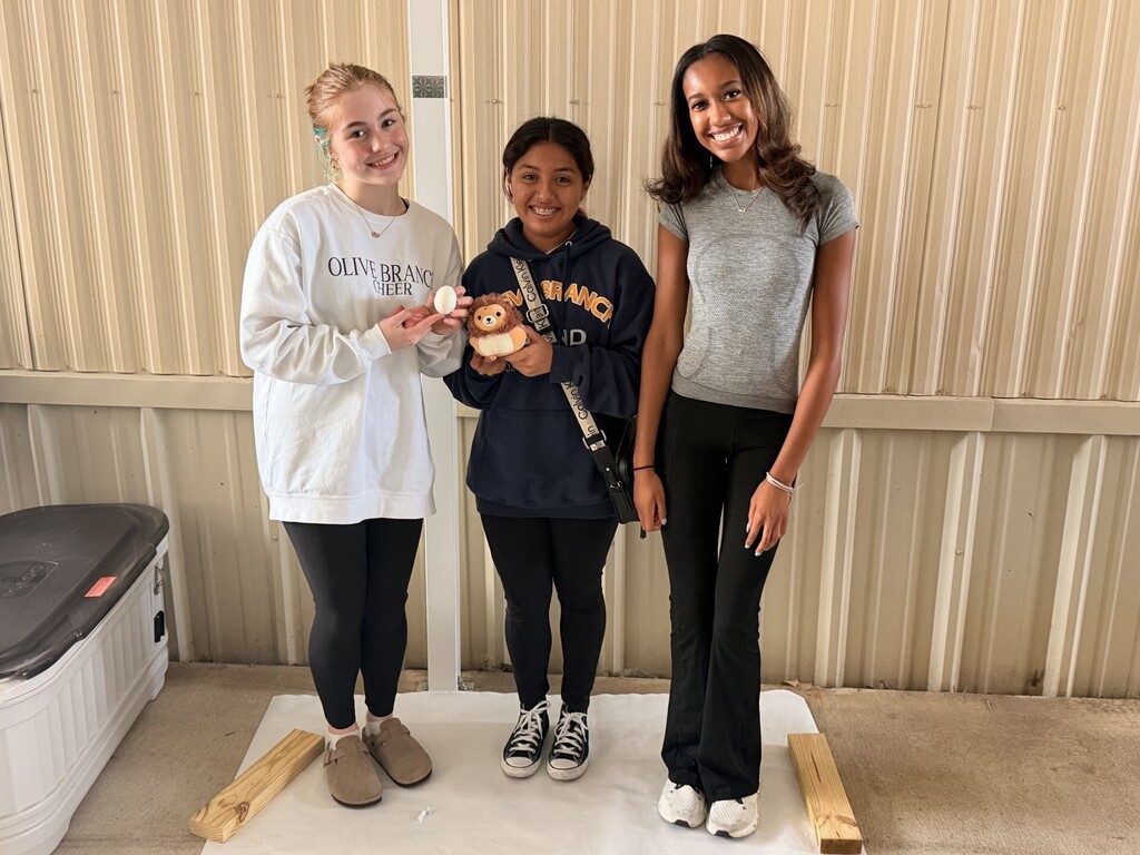 three students posing showing their egg