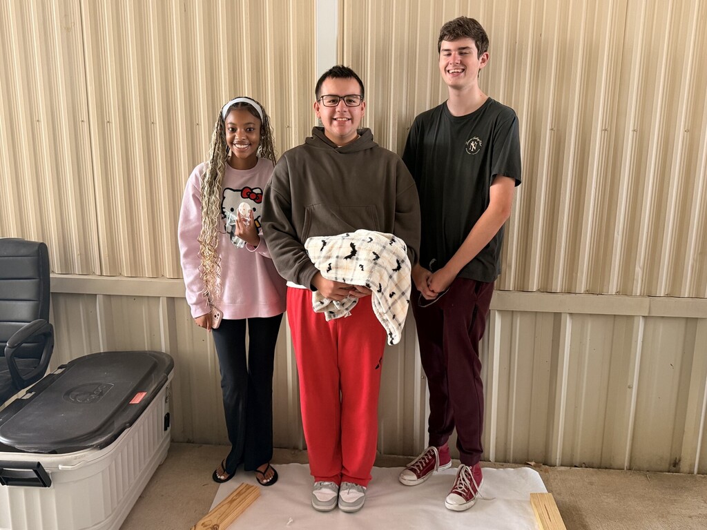 three students posing showing their egg