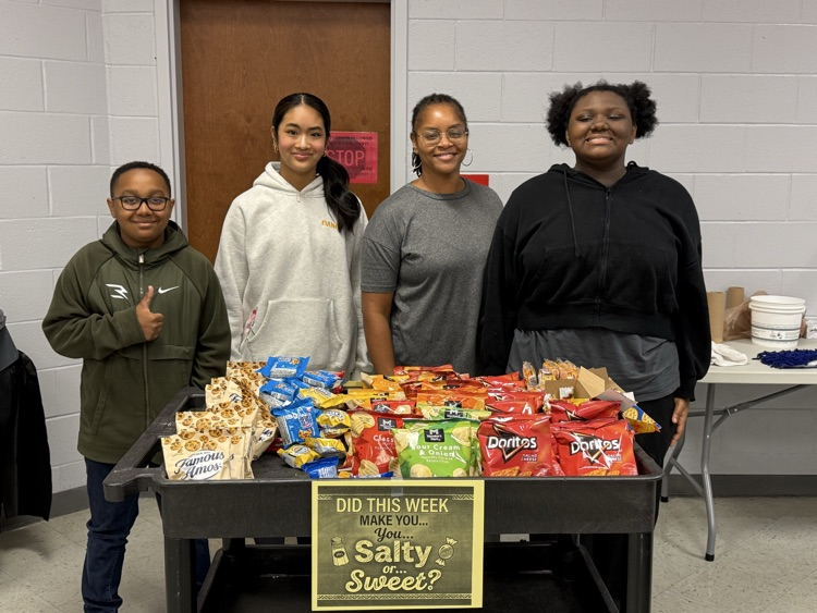Three students and one teacher standing behind a snack cart with a sign that says “Did this week make you salty or sweet?"