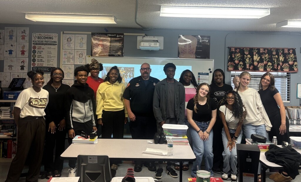 class of students posing for picture with firefighter