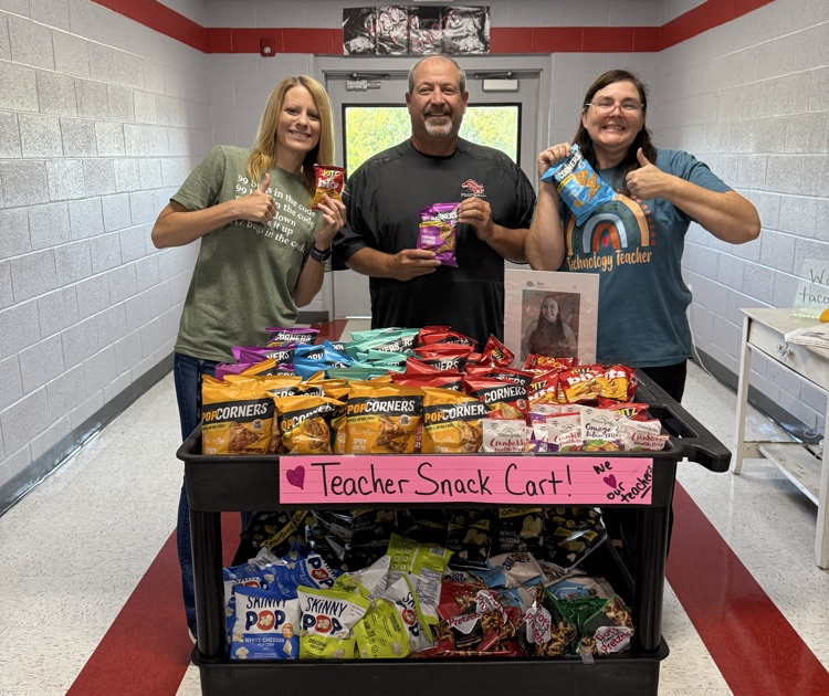 Three teachers standing behind a Teacher Snack Cart filled with snacks.