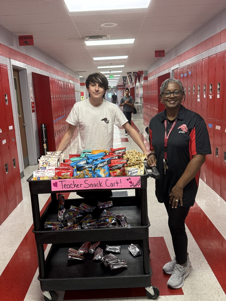 image shows Logan B. and Mrs. Sharp standing with the Teacher Snack Cart loaded down with goodies.