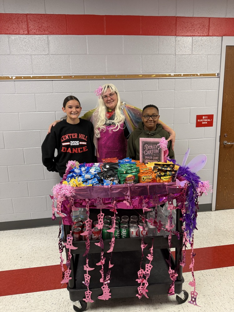 image shows a snack cart decorated in pink streamers and a Teacher wearing a blonde wig with two students.