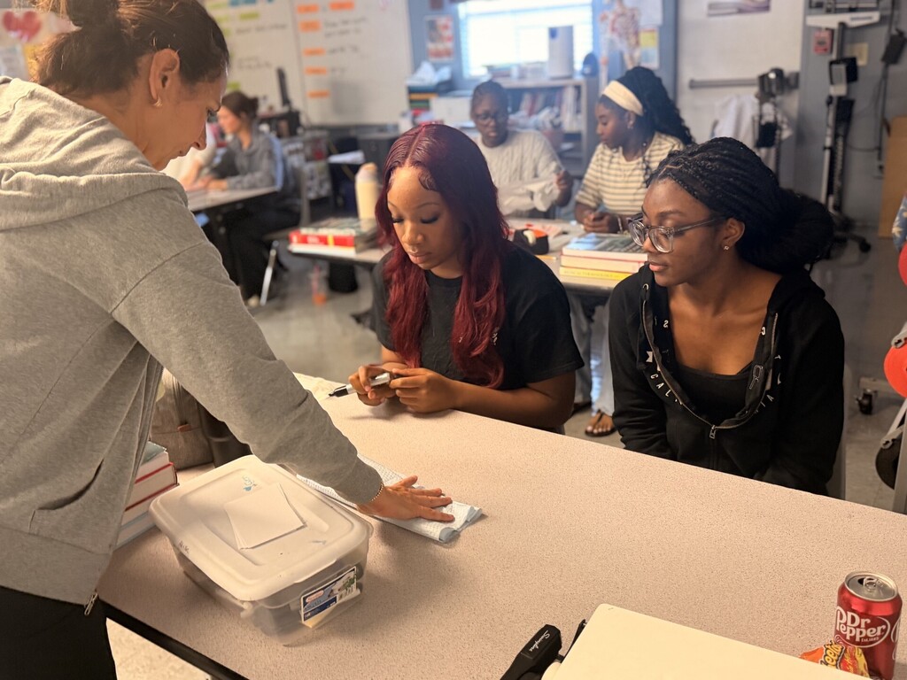 teacher showing two students practicing sterile wrapping