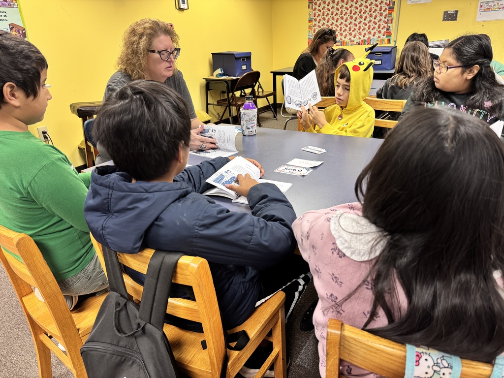 picture of kids and adults sitting around a table reading a book 