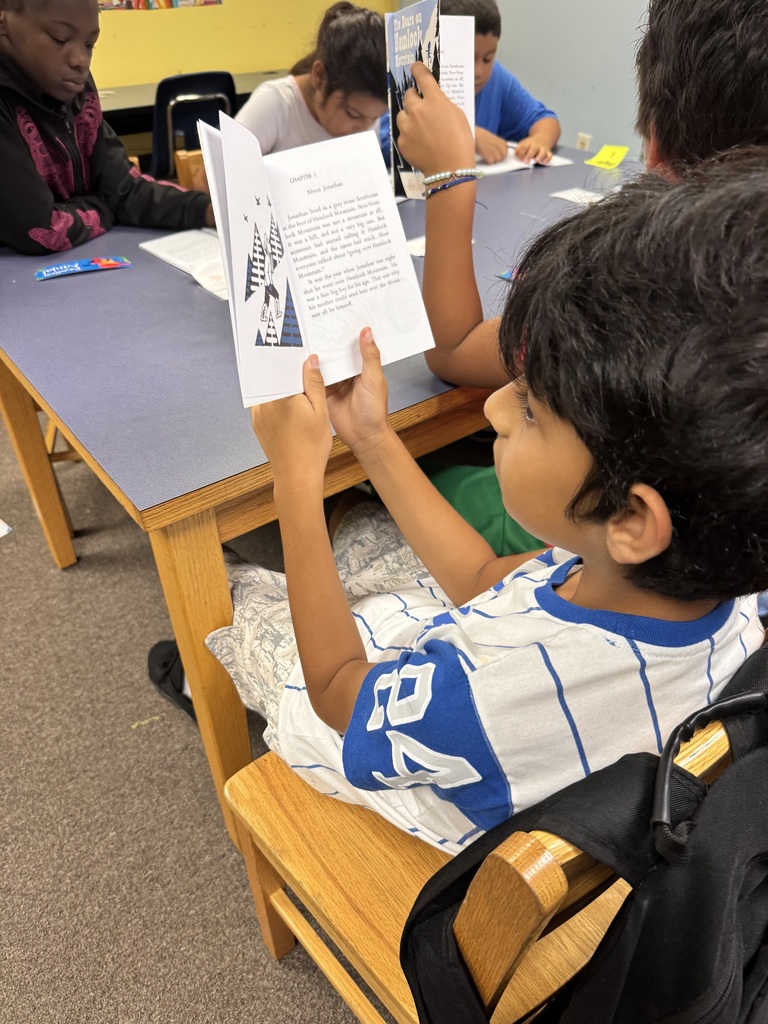 picture of kids and adults sitting around a table reading a book 
