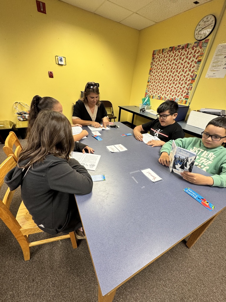 picture of kids and adults sitting around a table reading a book 