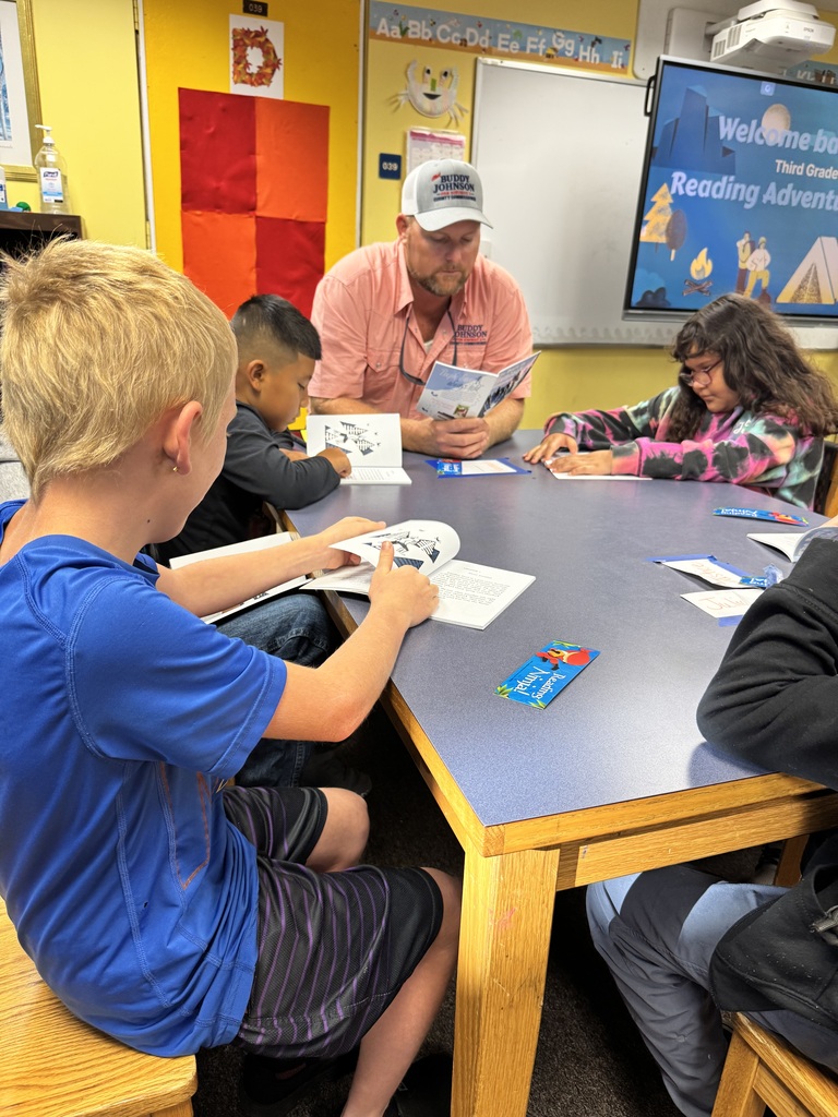 picture of kids and adults sitting around a table reading a book 