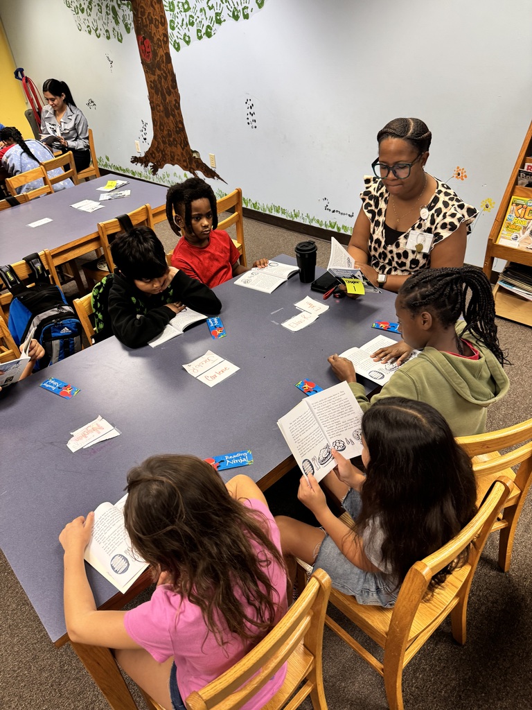 picture of kids and adults sitting around a table reading a book 