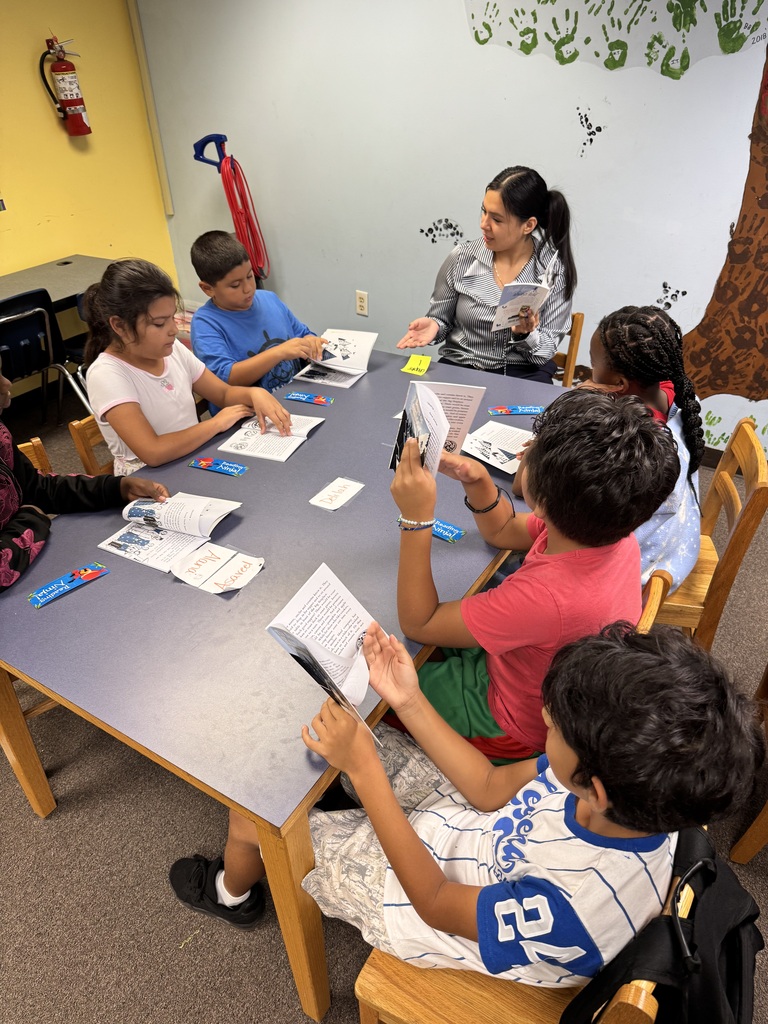 picture of kids and adults sitting around a table reading a book 