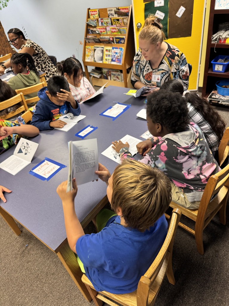 picture of kids and adults sitting around a table reading a book 