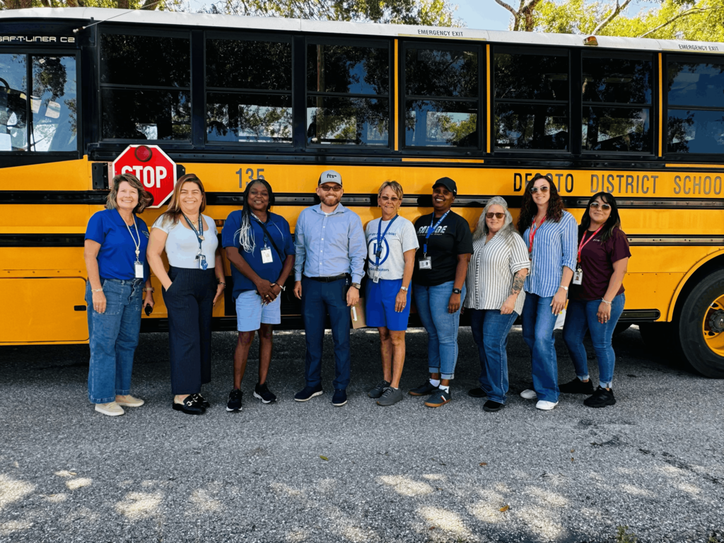 group of men and women smiling in front of a school bus