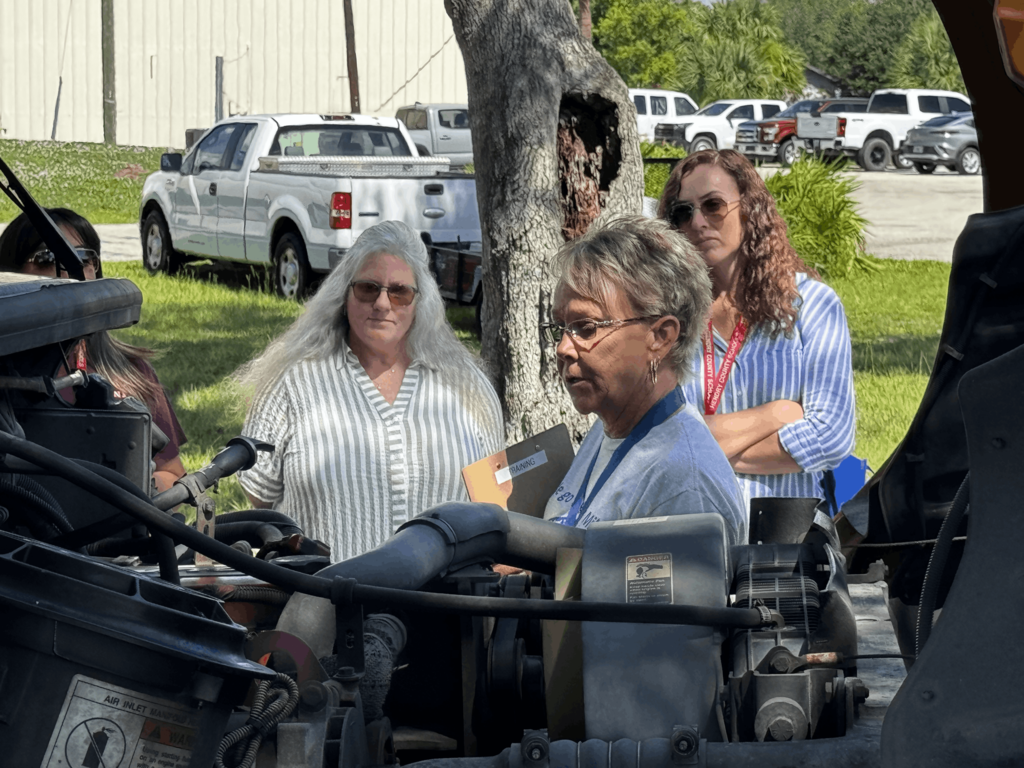 picture of woman showing 3 other women how to check under the hood of a bus