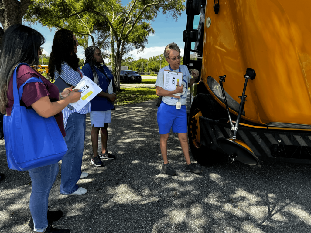 picture of woman showing 3 other women how to check under the hood of a bus