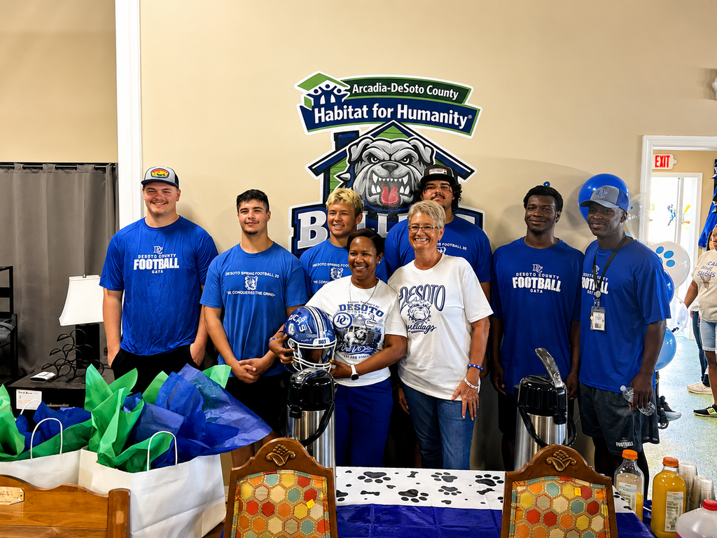 group of football player, coach, an 2 ladies wearing bulldog blue and posing for a picture