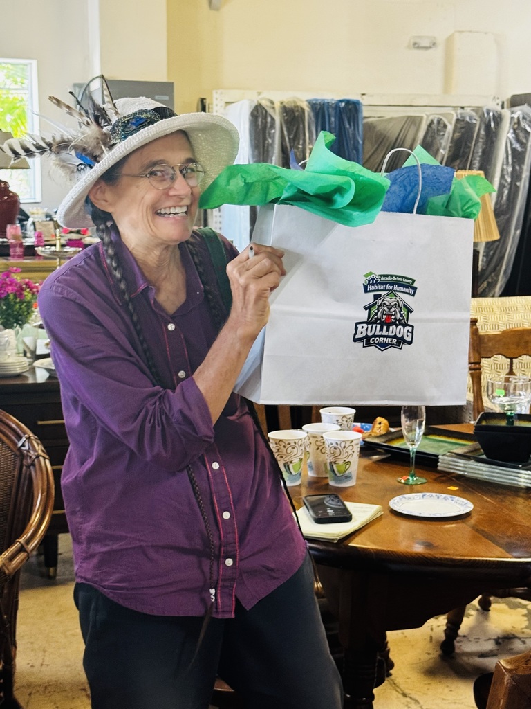 woman wearing a hat smiling and holding a gift bag